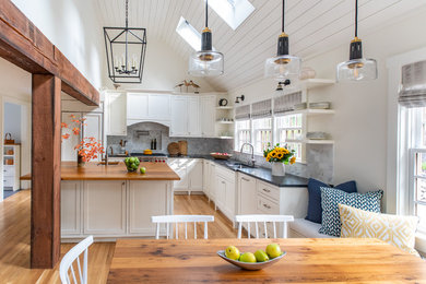 This is an example of a mid-sized country eat-in kitchen in Boston with a drop-in sink, recessed-panel cabinets, white cabinets, grey splashback, marble splashback, stainless steel appliances, medium hardwood floors, with island and black benchtop.