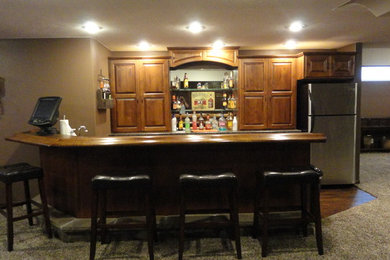 Example of a mid-sized classic galley medium tone wood floor and brown floor seated home bar design in Other with raised-panel cabinets, medium tone wood cabinets and wood countertops