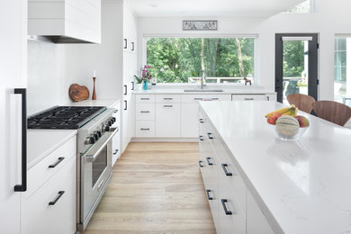Photo of a large modern l-shaped eat-in kitchen in Minneapolis with an undermount sink, flat-panel cabinets, white cabinets, white appliances, light hardwood floors, with island and brown floor.