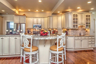 Eat-in kitchen - large transitional medium tone wood floor eat-in kitchen idea in Denver with a drop-in sink, raised-panel cabinets, white cabinets, granite countertops, beige backsplash, stone tile backsplash, stainless steel appliances and an island