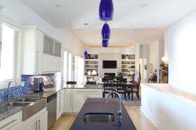 Trendy l-shaped kitchen photo in Little Rock with a farmhouse sink, flat-panel cabinets, white cabinets, granite countertops, blue backsplash, porcelain backsplash and stainless steel appliances