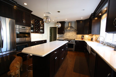 Photo of a large traditional u-shaped kitchen in New York with a belfast sink, shaker cabinets, dark wood cabinets, engineered stone countertops, multi-coloured splashback, matchstick tiled splashback, stainless steel appliances, medium hardwood flooring, an island and brown floors.