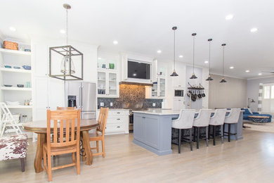 Inspiration for a mid-sized arts and crafts single-wall eat-in kitchen in Atlanta with a single-bowl sink, shaker cabinets, white cabinets, quartz benchtops, black splashback, stone tile splashback, stainless steel appliances, light hardwood floors and with island.