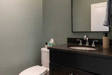 Powder room - mid-sized contemporary vinyl floor and brown floor powder room idea in Other with shaker cabinets, black cabinets, a two-piece toilet, green walls, an undermount sink, solid surface countertops, black countertops and a freestanding vanity