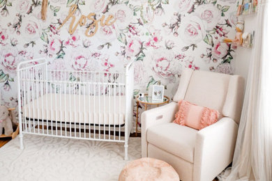 Diseño de habitación de bebé niña actual de tamaño medio con paredes blancas, suelo de madera en tonos medios, suelo marrón y papel pintado