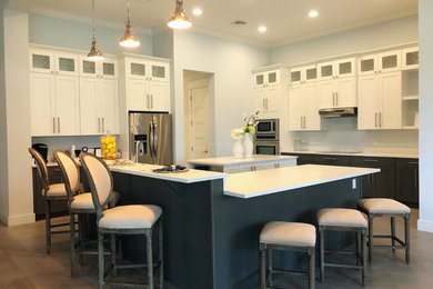Mid-sized trendy medium tone wood floor and brown floor open concept kitchen photo in Orlando with an undermount sink, shaker cabinets, white cabinets, quartz countertops, white backsplash, stainless steel appliances, two islands and white countertops