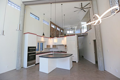 Open concept kitchen - contemporary l-shaped concrete floor and gray floor open concept kitchen idea in Edmonton with an undermount sink, flat-panel cabinets, white cabinets, quartz countertops, white backsplash, glass tile backsplash, stainless steel appliances, an island and black countertops