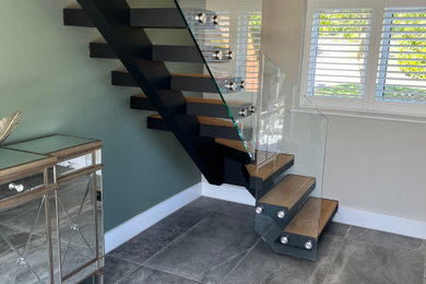 Medium sized contemporary wood l-shaped glass railing staircase in Essex with open risers.