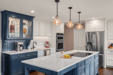 Inspiration for a mid-sized french country u-shaped dark wood floor and brown floor kitchen remodel in Seattle with an undermount sink, recessed-panel cabinets, blue cabinets, quartz countertops, white backsplash, porcelain backsplash, stainless steel appliances, an island and white countertops