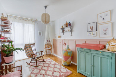Exemple d'une chambre de bébé fille éclectique de taille moyenne avec un mur rose, un sol en bois brun et un sol marron.