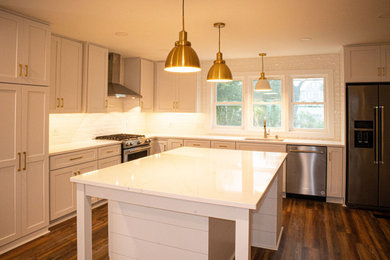 Example of a large beach style l-shaped brown floor open concept kitchen design in Other with an undermount sink, recessed-panel cabinets, white cabinets, quartz countertops, white backsplash, subway tile backsplash, stainless steel appliances, an island and white countertops