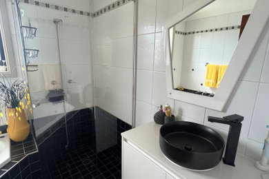 This is an example of a mid-sized eclectic master bathroom in Sydney with flat-panel cabinets, white cabinets, a hot tub, a corner shower, a one-piece toilet, black and white tile, ceramic tile, white walls, ceramic floors, a vessel sink, engineered quartz benchtops, black floor, a hinged shower door, white benchtops, a single vanity and a freestanding vanity.