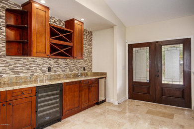 Wet bar - mid-sized traditional single-wall beige floor wet bar idea in Phoenix with an undermount sink, shaker cabinets, dark wood cabinets, granite countertops, multicolored backsplash and brown countertops
