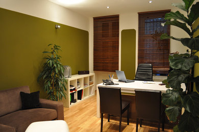 Großes Modernes Arbeitszimmer mit Arbeitsplatz, grüner Wandfarbe, braunem Holzboden, freistehendem Schreibtisch und braunem Boden in Berlin