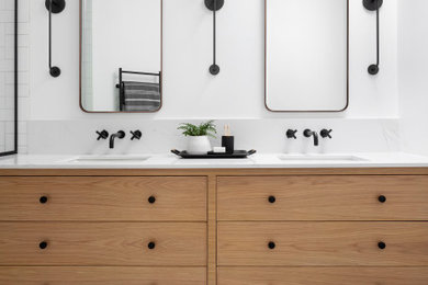 This is an example of a mid-sized scandinavian kids bathroom in Montreal with light wood cabinets, an alcove shower, a one-piece toilet, white tile, ceramic tile, white walls, mosaic tile floors, an undermount sink, engineered quartz benchtops, black floor, a hinged shower door, white benchtops, a niche, a double vanity, a built-in vanity and flat-panel cabinets.