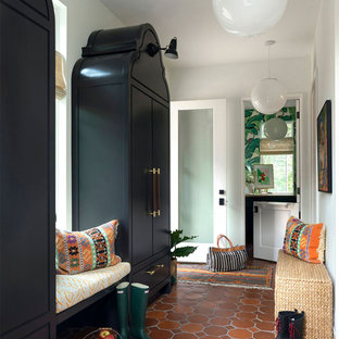 Idée de décoration pour une entrée bohème avec un vestiaire, un mur blanc, un sol en carreau de terre cuite, une porte en verre et un sol orange.