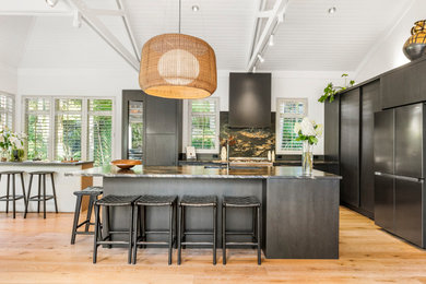 Photo of a contemporary l-shaped kitchen/diner in Auckland with a double-bowl sink, flat-panel cabinets, dark wood cabinets, granite worktops, black splashback, stone slab splashback, black appliances, laminate floors, an island, black worktops and exposed beams.