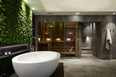 This is an example of a large contemporary bathroom in Cologne with flat-panel cabinets, dark wood cabinets, a freestanding tub, a curbless shower, a two-piece toilet, gray tile, ceramic tile, black walls, ceramic floors, with a sauna, a trough sink, grey floor, an open shower and black benchtops.