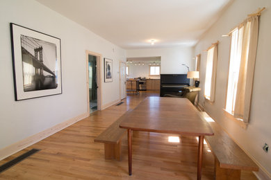 Eat-in kitchen - mid-sized 1950s galley light wood floor and multicolored floor eat-in kitchen idea in New York with a drop-in sink, flat-panel cabinets, light wood cabinets, quartzite countertops, white backsplash, porcelain backsplash, stainless steel appliances, an island and black countertops