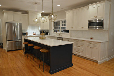 Inspiration for a large transitional l-shaped medium tone wood floor and brown floor open concept kitchen remodel in New York with an undermount sink, recessed-panel cabinets, white cabinets, quartzite countertops, white backsplash, marble backsplash, stainless steel appliances, an island and white countertops