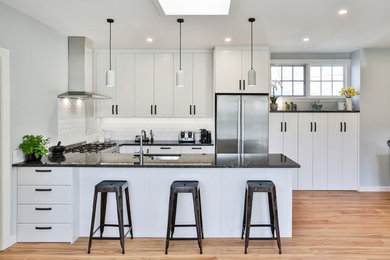 Inspiration for a mid-sized transitional u-shaped eat-in kitchen in Christchurch with an undermount sink, white cabinets, granite benchtops, white splashback, subway tile splashback, stainless steel appliances, medium hardwood floors, black benchtop, shaker cabinets, a peninsula and beige floor.