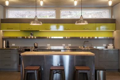 Photo of an industrial l-shaped kitchen in Vancouver with an integrated sink, flat-panel cabinets, grey cabinets, stainless steel benchtops, stainless steel appliances, with island, grey floor and grey benchtop.