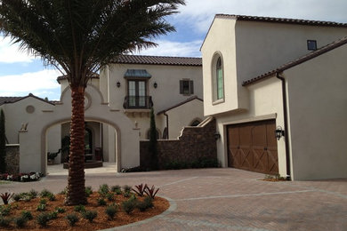 This is an example of an expansive mediterranean two-storey beige exterior in Tampa with stone veneer and a gable roof.