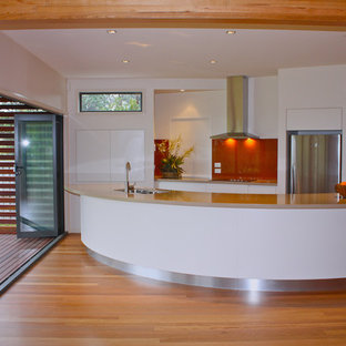 Inredning av ett modernt litet beige beige kök, med en nedsänkt diskho, släta luckor, vita skåp, bänkskiva i kvarts, rött stänkskydd, glaspanel som stänkskydd, rostfria vitvaror, mellanmörkt trägolv och en köksö