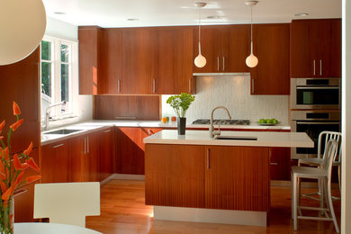 Example of a mid-century modern l-shaped medium tone wood floor kitchen design in Los Angeles with flat-panel cabinets, medium tone wood cabinets, an island, a single-bowl sink, solid surface countertops, white backsplash, ceramic backsplash and stainless steel appliances