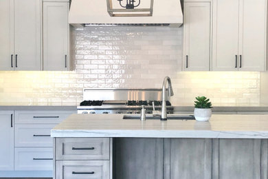 Example of a large transitional l-shaped medium tone wood floor, brown floor and vaulted ceiling open concept kitchen design in Phoenix with a single-bowl sink, shaker cabinets, gray cabinets, quartzite countertops, white backsplash, ceramic backsplash, stainless steel appliances and an island