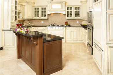 This is an example of a traditional u-shaped kitchen in Toronto with stainless steel appliances, with island, raised-panel cabinets and light wood cabinets.