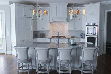 Open concept kitchen - mid-sized traditional galley medium tone wood floor open concept kitchen idea in Raleigh with a farmhouse sink, recessed-panel cabinets, white cabinets, granite countertops, white backsplash, stone tile backsplash, paneled appliances and an island