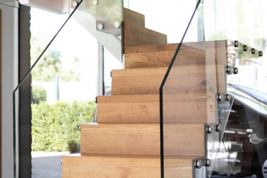 Пример оригинального дизайна: большая п-образная деревянная лестница в современном стиле с деревянными ступенями и стеклянными перилами