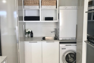 This is an example of a small contemporary galley utility room in Perth with an undermount sink, flat-panel cabinets, grey cabinets, quartz benchtops, grey walls, porcelain floors, a concealed washer and dryer and grey floor.