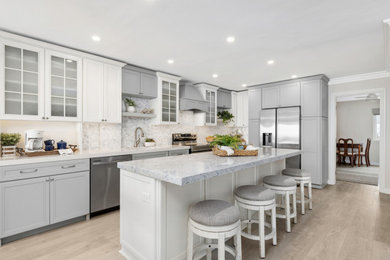 Open concept kitchen - large coastal l-shaped vinyl floor and beige floor open concept kitchen idea in San Diego with an undermount sink, shaker cabinets, white cabinets, quartz countertops, gray backsplash, glass tile backsplash, stainless steel appliances, an island and black countertops
