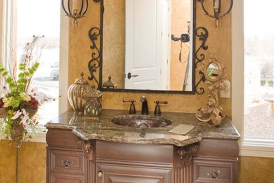 This is an example of a mid-sized mediterranean 3/4 bathroom in Indianapolis with an undermount sink, furniture-like cabinets, medium wood cabinets, granite benchtops, a two-piece toilet, multi-coloured tile, multi-coloured walls and travertine floors.