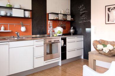 Ejemplo de cocina lineal contemporánea de tamaño medio abierta con puertas de armario blancas, encimera de acero inoxidable y salpicadero naranja