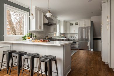 Inspiration for a mid-sized transitional u-shaped medium tone wood floor and brown floor eat-in kitchen remodel in Newark with a farmhouse sink, shaker cabinets, white cabinets, quartz countertops, gray backsplash, marble backsplash, stainless steel appliances, a peninsula and white countertops