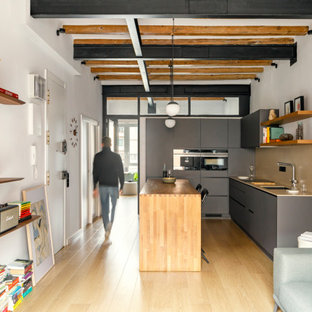 Ejemplo de cocina comedor en L, industrial, de tamaño medio, con fregadero bajoencimera, armarios con paneles lisos, puertas de armario grises, encimera de cuarcita, salpicadero beige, salpicadero de azulejos de cerámica, electrodomésticos negros, suelo laminado, una isla, suelo marrón y encimeras beige