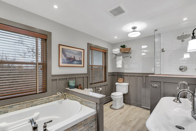 Photo of a medium sized classic ensuite bathroom in New York with a built-in bath, a double shower, a two-piece toilet, white tiles, cement tiles, grey walls, wood-effect flooring, a trough sink, beige floors, a hinged door, double sinks, a floating vanity unit and wainscoting.