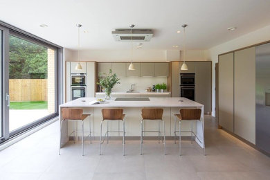 Inspiration for a large modern l-shaped eat-in kitchen in Oxfordshire with flat-panel cabinets, quartzite benchtops, glass sheet splashback, stainless steel appliances and with island.