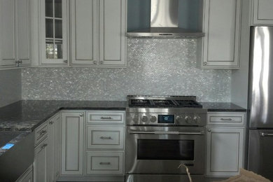 Mid-sized transitional kitchen photo in New York with a farmhouse sink, recessed-panel cabinets, white cabinets, granite countertops, metallic backsplash, metal backsplash, stainless steel appliances and an island