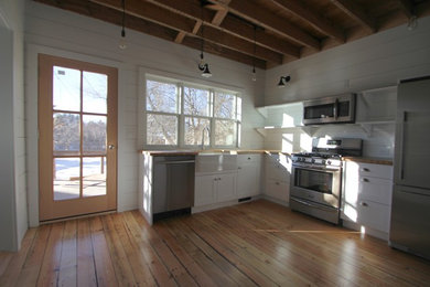 Eat-in kitchen - farmhouse l-shaped eat-in kitchen idea in Other with a farmhouse sink, flat-panel cabinets, white cabinets, wood countertops, white backsplash and stainless steel appliances
