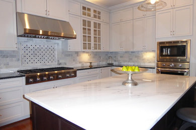 Example of a mid-sized minimalist u-shaped medium tone wood floor and brown floor open concept kitchen design in DC Metro with white cabinets, white backsplash, an island, a farmhouse sink, recessed-panel cabinets, marble countertops, marble backsplash and stainless steel appliances