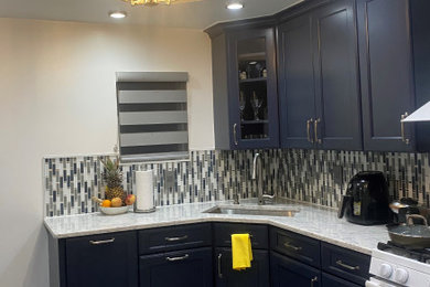 Kitchen - transitional l-shaped porcelain tile, multicolored floor and tray ceiling kitchen idea in New York with an undermount sink, recessed-panel cabinets, blue cabinets, quartz countertops, multicolored backsplash, glass sheet backsplash, white appliances, no island and multicolored countertops