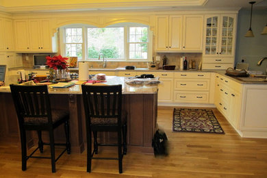 Huge elegant u-shaped medium tone wood floor enclosed kitchen photo in Other with white cabinets, granite countertops, beige backsplash, stainless steel appliances, an island, a single-bowl sink, recessed-panel cabinets and subway tile backsplash