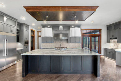 Photo of a large u-shaped kitchen in Milwaukee with a farmhouse sink, shaker cabinets, grey cabinets, granite benchtops, grey splashback, stone tile splashback, stainless steel appliances, medium hardwood floors, with island, brown floor, grey benchtop and coffered.