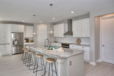 Inspiration for a mid-sized coastal l-shaped light wood floor and beige floor open concept kitchen remodel in Jacksonville with an undermount sink, recessed-panel cabinets, white cabinets, granite countertops, white backsplash, subway tile backsplash, stainless steel appliances, an island and multicolored countertops
