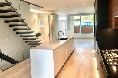 Open concept kitchen - mid-sized modern single-wall light wood floor and beige floor open concept kitchen idea in Seattle with an undermount sink, flat-panel cabinets, black cabinets, solid surface countertops, black backsplash, black appliances, an island and black countertops