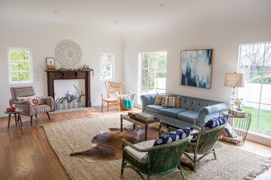 Inspiration for a mid-sized eclectic open concept living room in San Diego with white walls, medium hardwood floors, a standard fireplace and a wood fireplace surround.